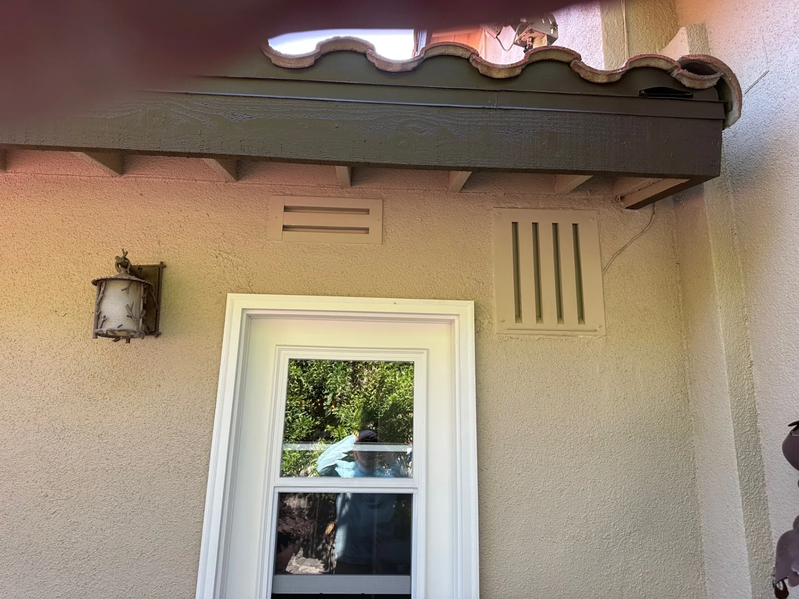Two ember-resistant vents installed in the cream stucco wall of a California home beneath a tile roof eave