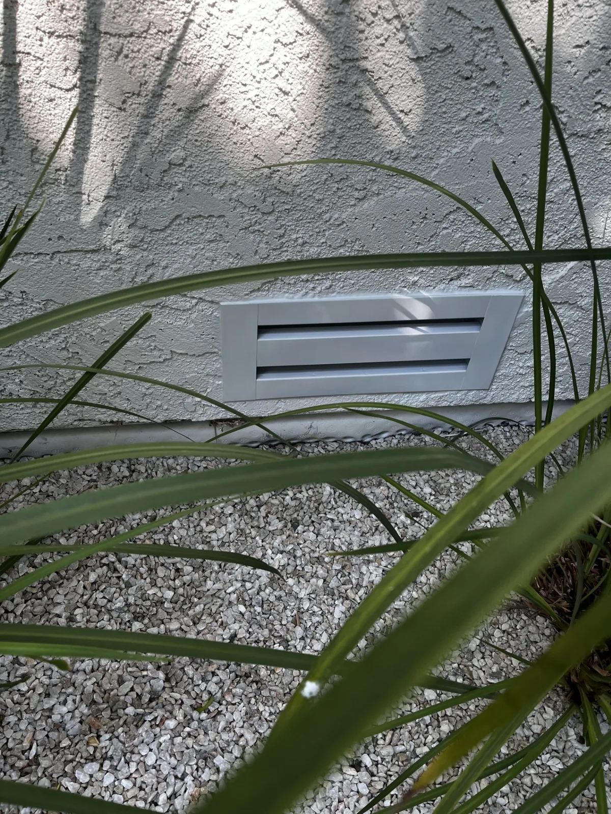 Ember-resistant foundation vent set into a stucco wall above landscaped gravel