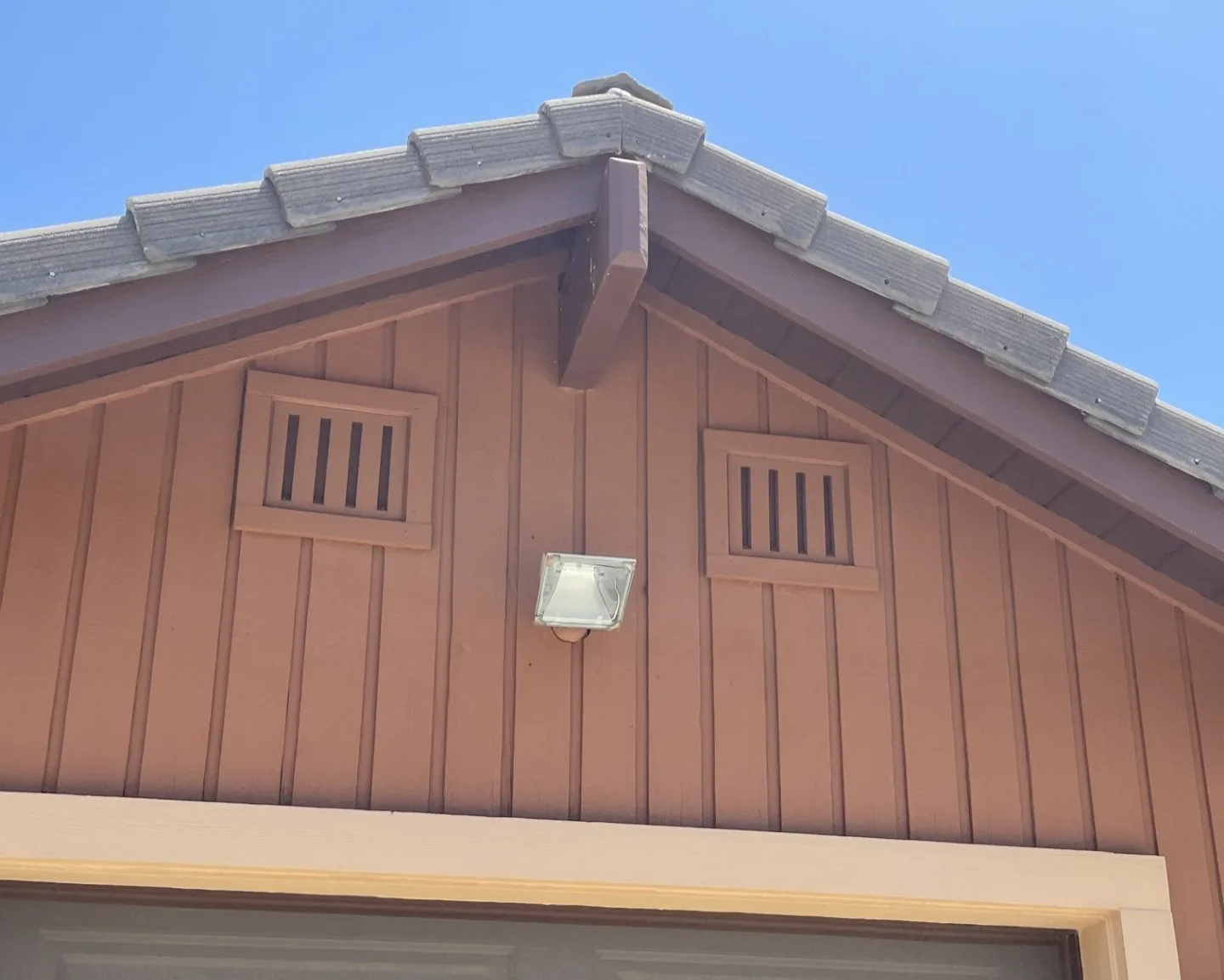 Two square ember-resistant gable vents on rust-brown board-and-batten siding under a tile roof