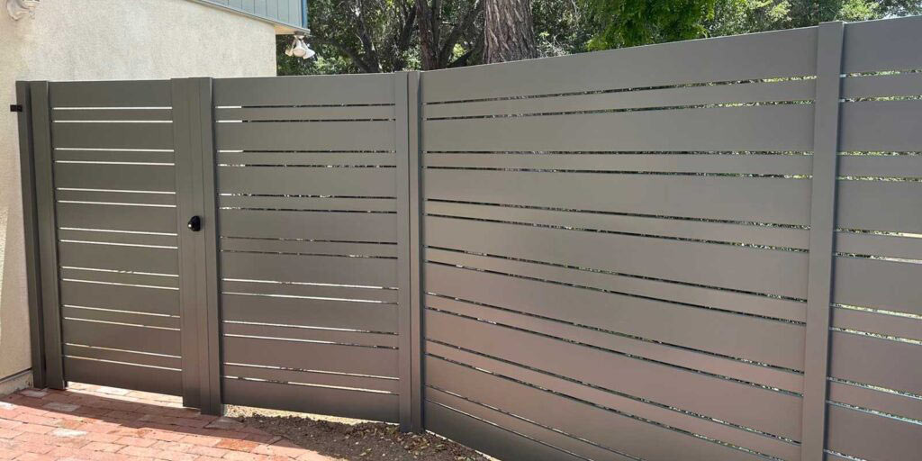 Bronze horizontal-slat aluminum fence and matching pedestrian gate at the side of a stucco home