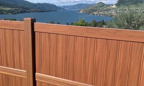 Cedar-tone woodgrain vinyl privacy fence overlooking a lake